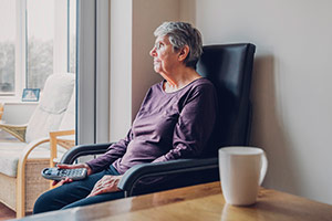 An elderly woman in a home suffering from financial abuse is staring out the window.