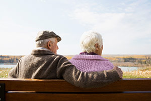 An elderly couple sitting close together looking out into the distance.